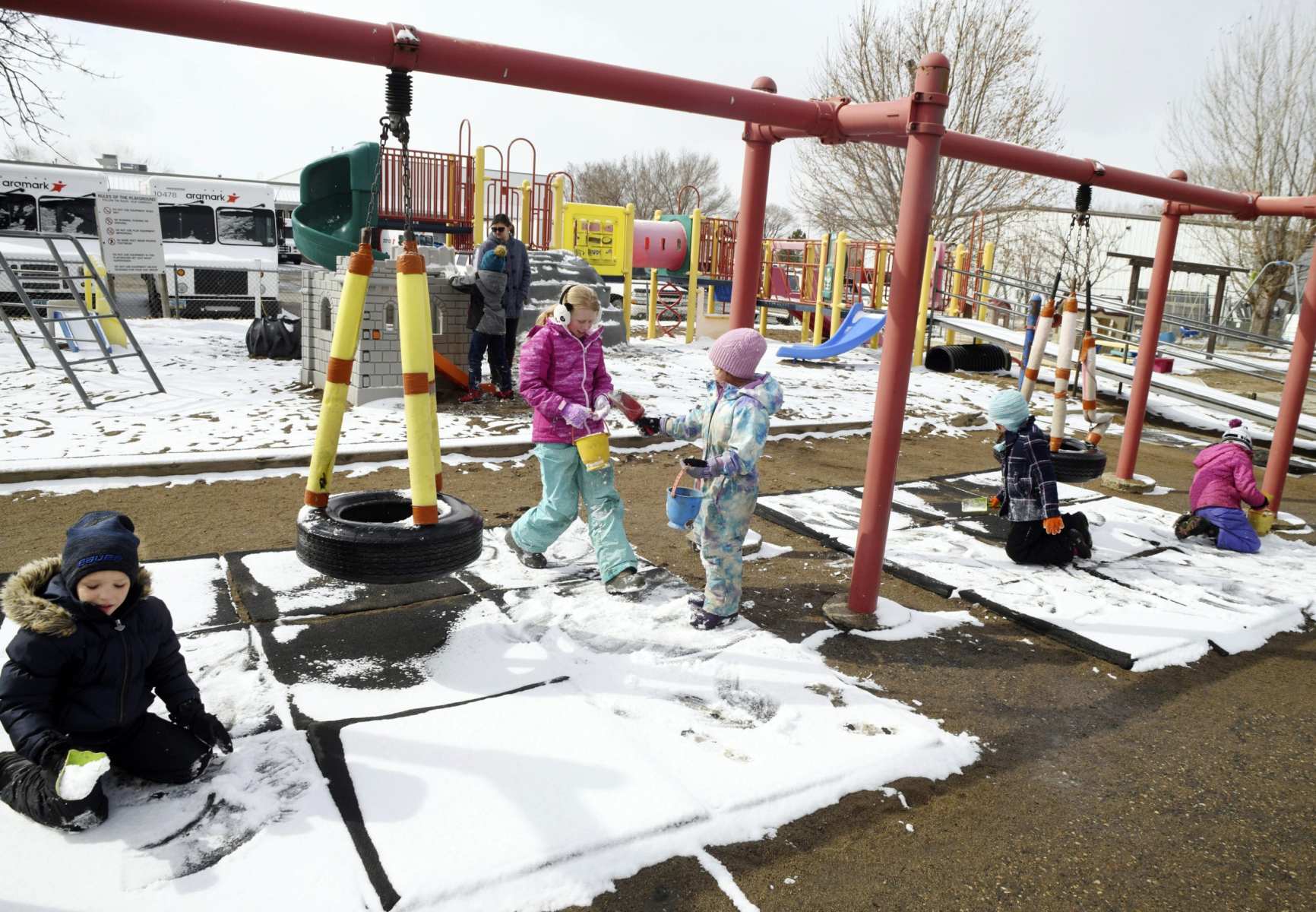 Children playing on a swing set with snow on the ground.