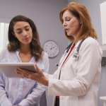 Mid aged medical doctor using portable tablet to review test results of patient.