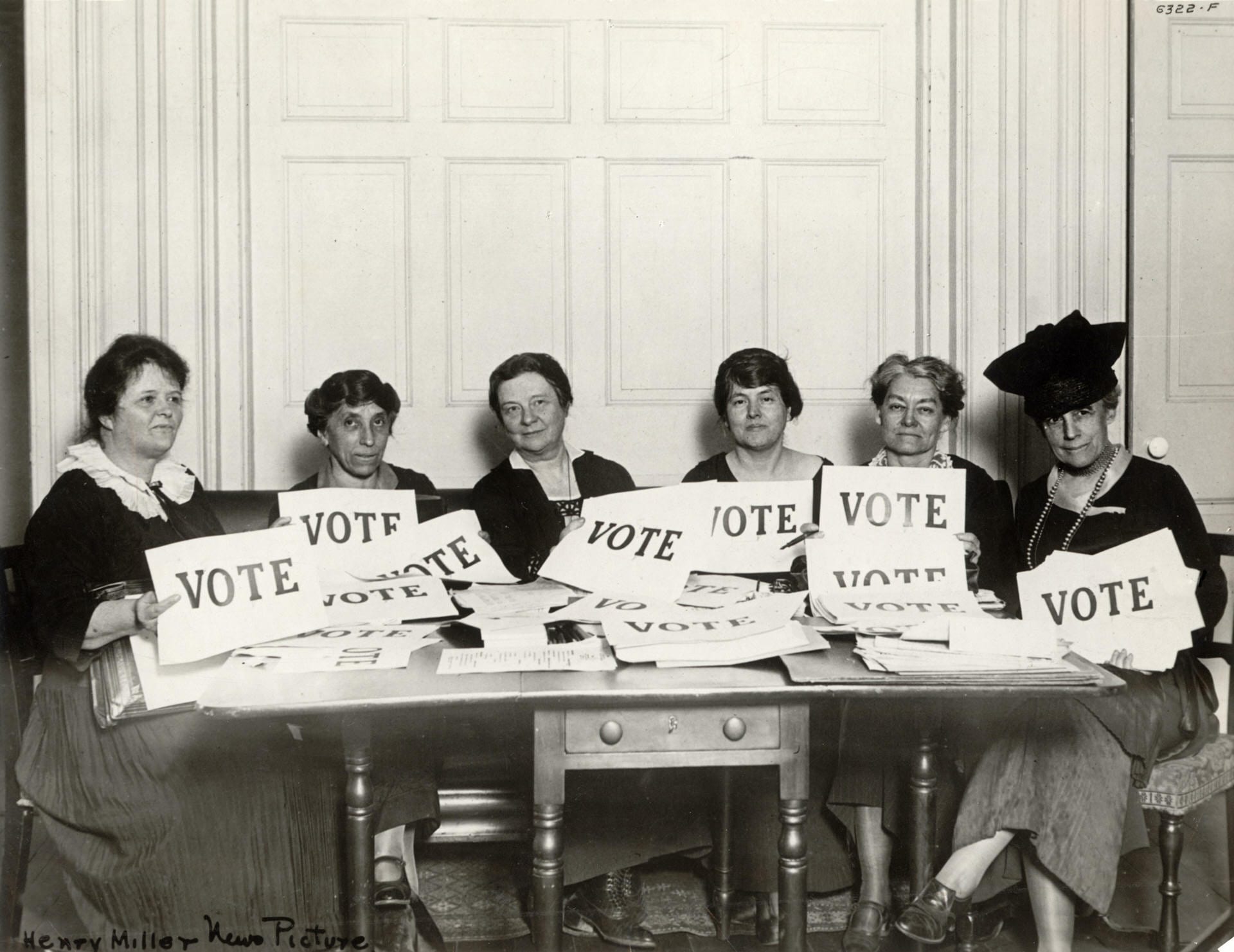 A group of women in a black and white photo hold signs that say "vote."