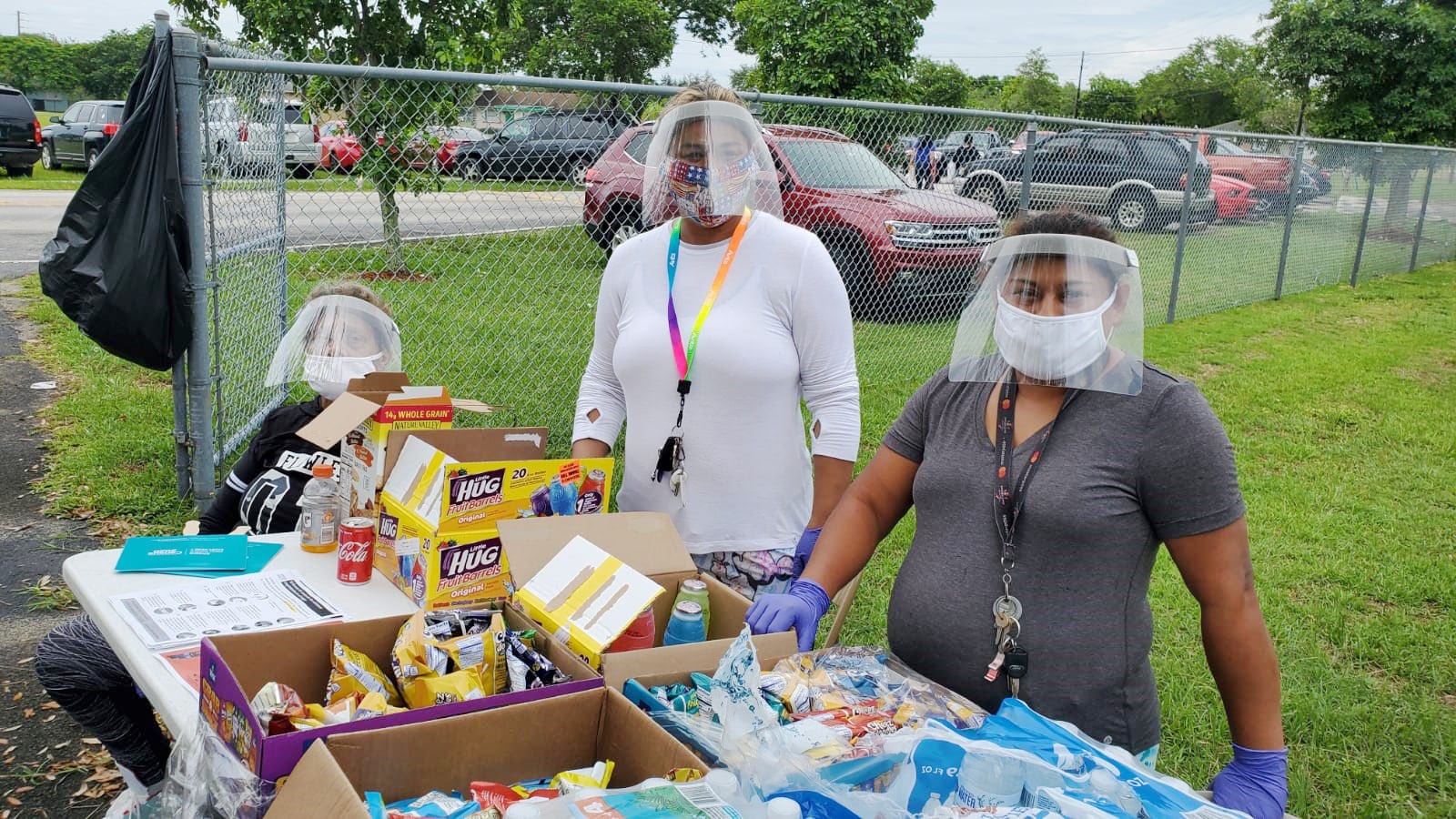 Three women wearing face shields passing out food.