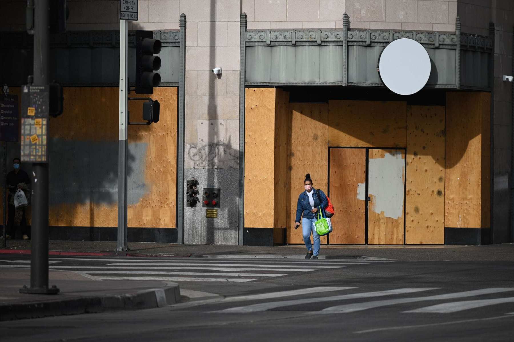 A woman wearing a facemask to prevent the spread of coronavirus walks past a boarded up storefront at the intersection of Hill Street and 5th Street in downtown Los Angeles, California, November 5, 2020 as the country awaits the result of the November 3 US presidential election. - Businesses in major US cities were boarded up in anticipation of unrest. The nail-biting US election was on the cusp of finally producing a winner Thursday, with Democrat Joe Biden declaring "no doubt" he would beat President Donald Trump and all eyes on the decisive state of Pennsylvania. (Photo by Robyn Beck / AFP)