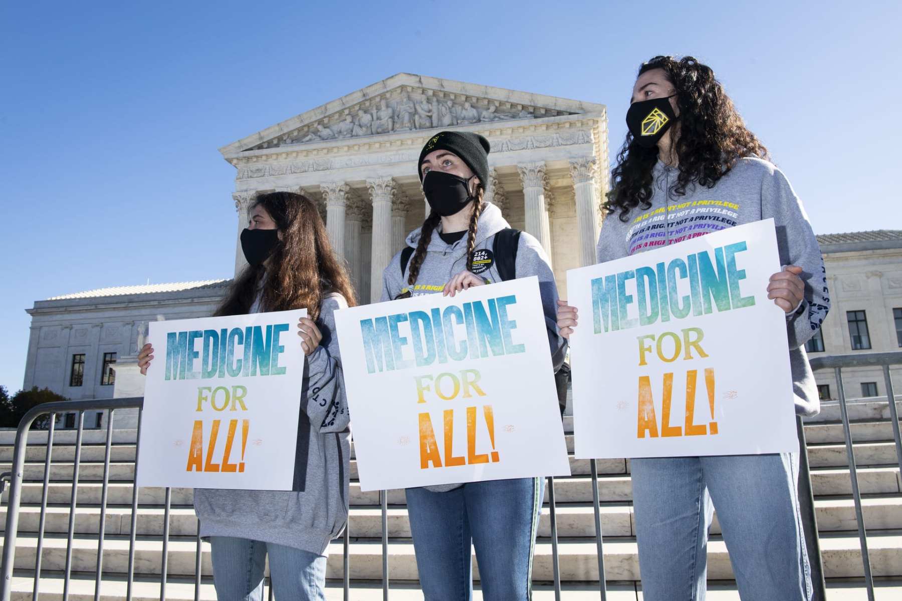 A group of people stand with signs that read "Medicine For All!"
