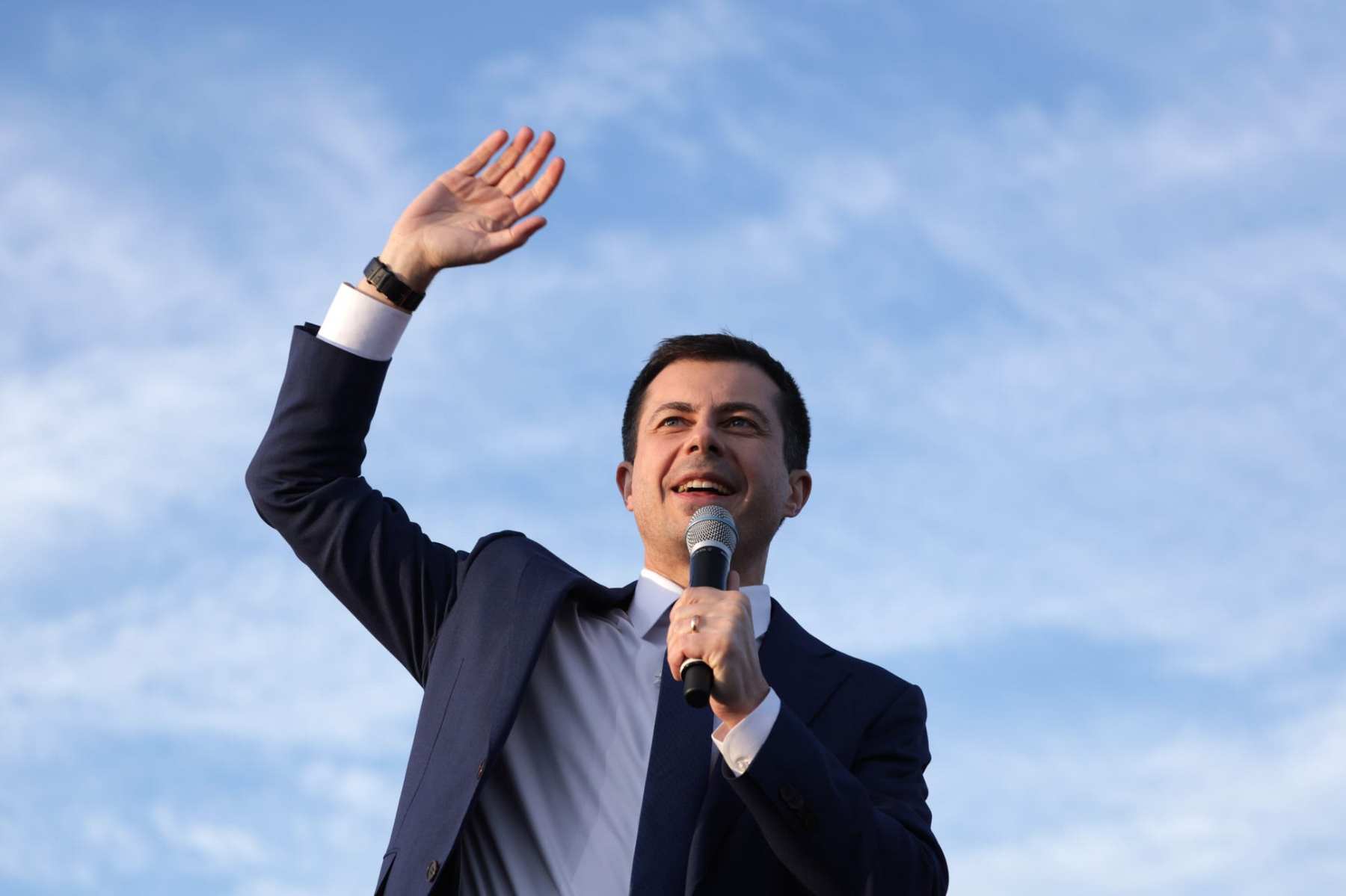 Pete Buttigieg waves while holding a microphone.