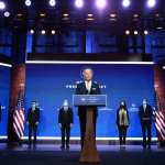 Biden standing at a podium surrounded by members of his Cabinet.