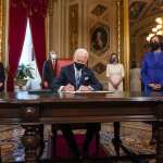 US President Joe Biden signs three documents at a table.