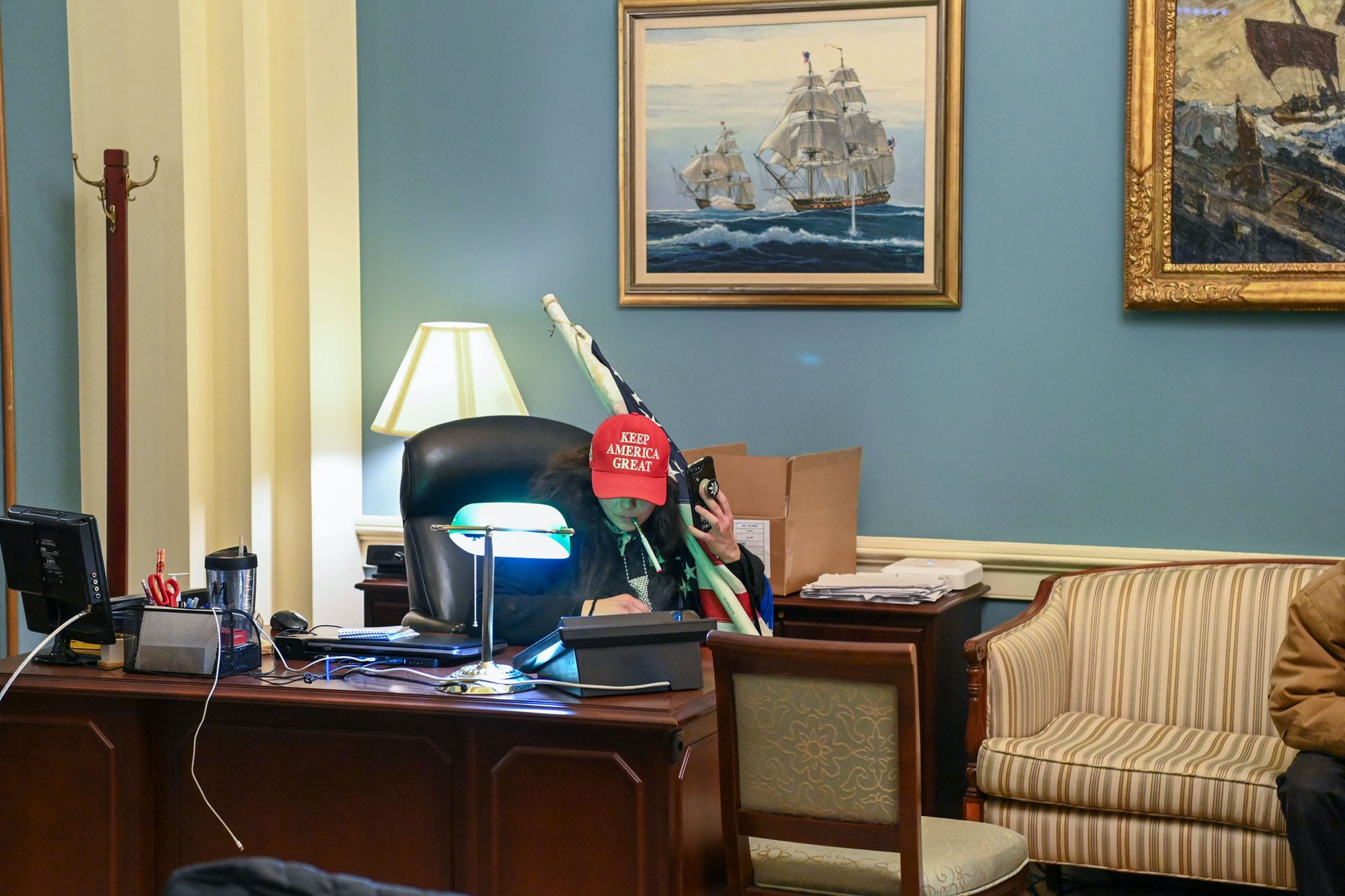 A woman sits at the desk of House Speaker Nancy Pelosi wearing a Make America Great Again hat.