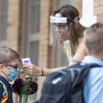 A student wearing a mask has his temperature checked as he enters a school.