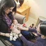 Midwife Lo Kawulok listens to the heartbeat of four week old Solene while her mother Summer Milacek holds her.