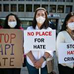 Asian community members hold signs calling for hate to stop.