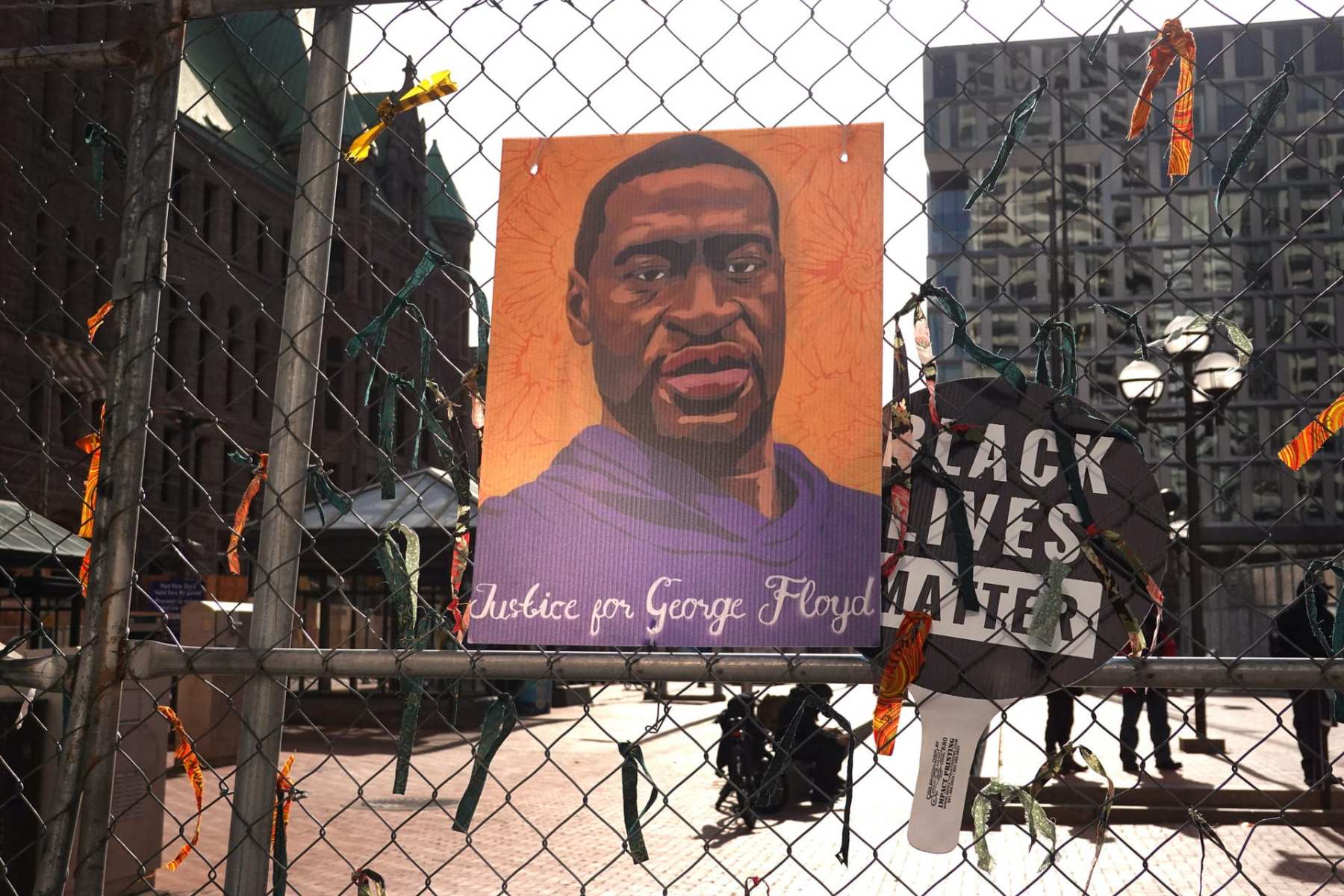 A illustration of George Floyd hangs on fencing next to a sign that reads "Black Lives Matter."