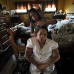 A home health aide brushes the hair of a patient in her home.