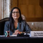 Deb Haaland sitting at a table speaking into a microphone.