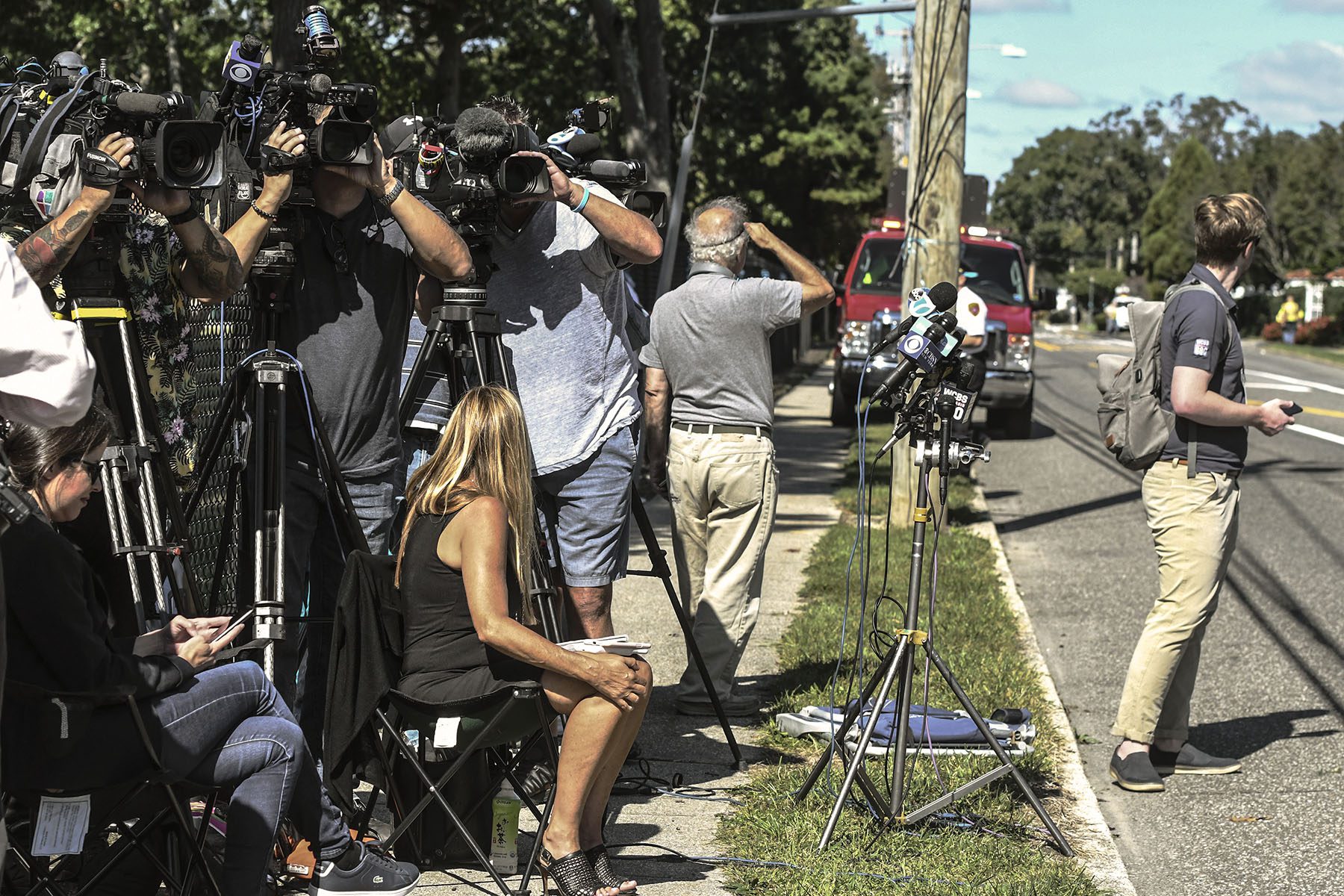 dozens of cameras and microphones, and press are seen on the side of a street.
