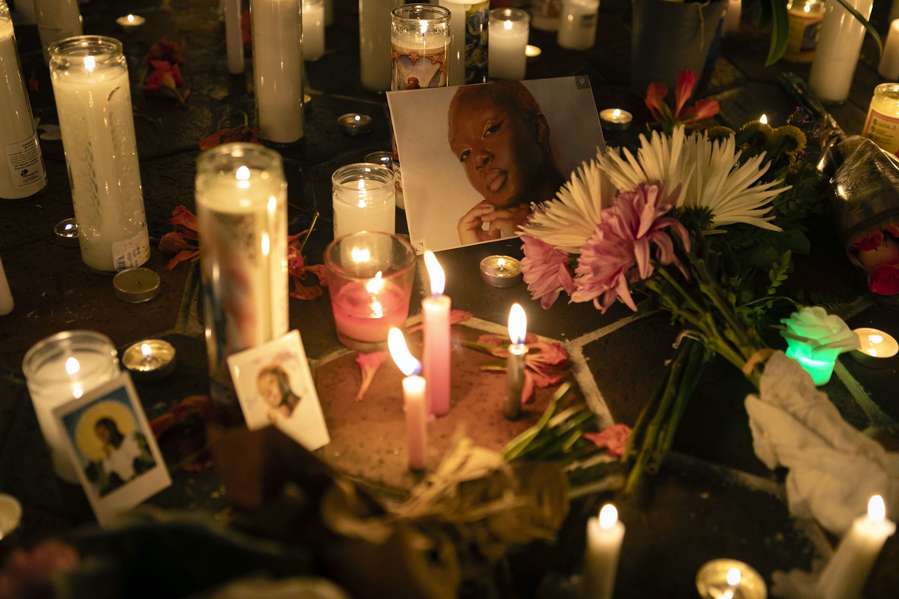 Flowers, lit candles and images of Toyin Salau are laid around the ground during a vigil.