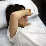 A pregnant woman covers her face while lying in a hospital bed.