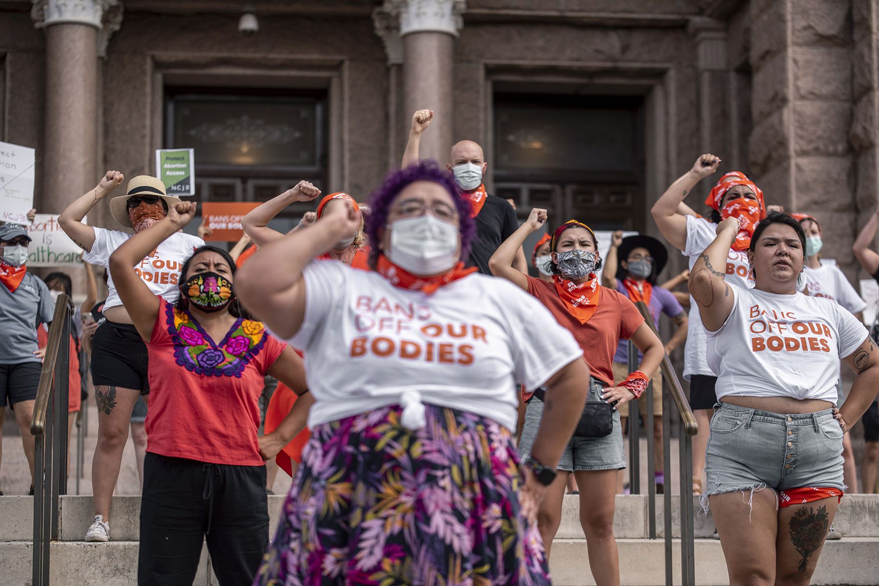 People wearing matching shirts that read "bans off our bodies" raise their fist in protest in front of the Texas State Capitol.