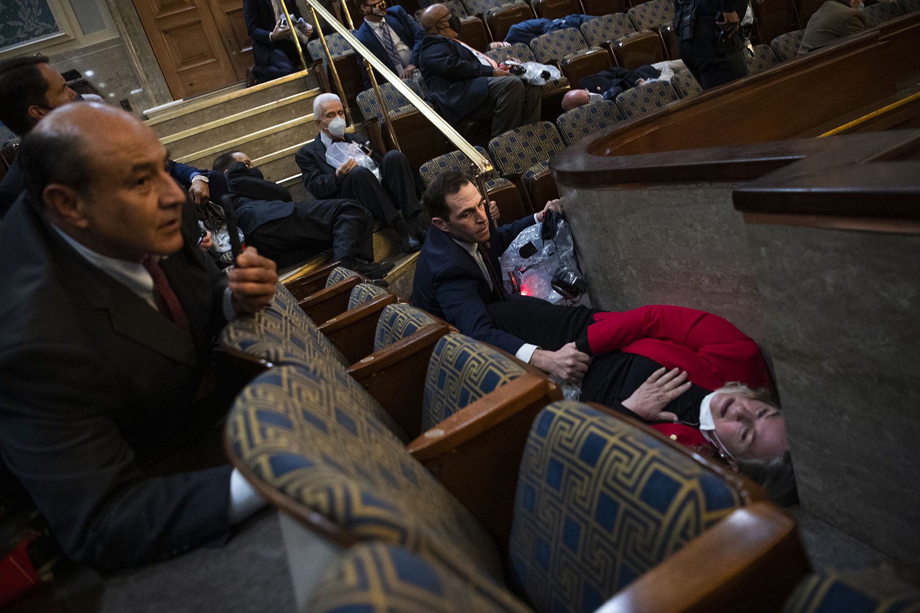 Rep. Susan Wild lays on the floor holding her hand over her heart while Rep. Jason Crow holds her hand to comfort her.