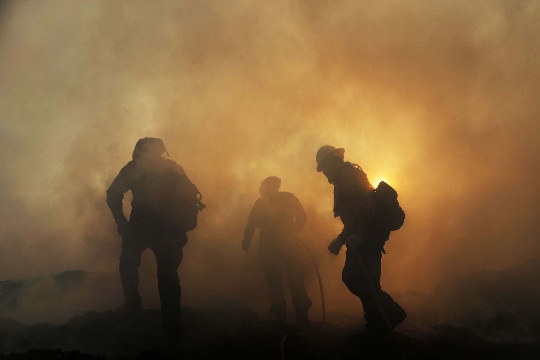 Three firefighters are seen enveloped in thick plumes of smoke.