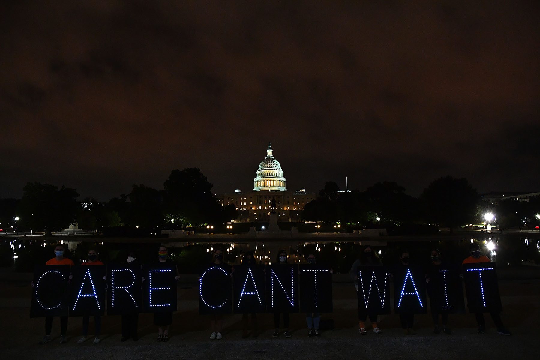 Activists hold neon signs that read "Care Can't Wait" while the U.S. Capitol Building is seen in the background.