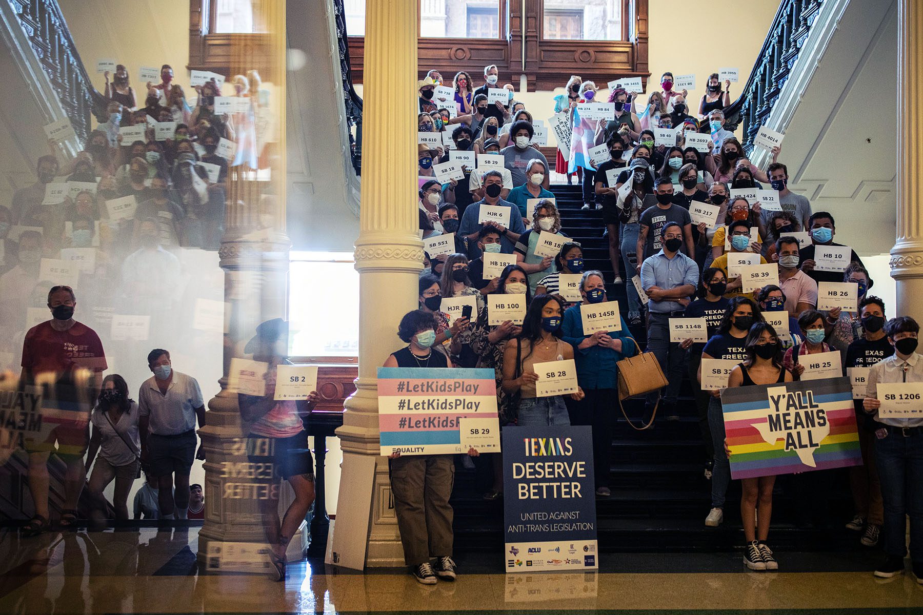 LGBTQ+ rights supporters inside the Texas State Capitol. Many hold signs, some read "Y'all Means All," "#LetKidsPlay.