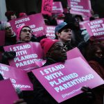 A diverse crowd of people hold signs that read 