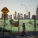 Pedestrians pass a 'dead end' sign before the Manhattan city skyline.