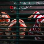 Three female inmates wearing orange and white striped prison uniforms sit on a bench.