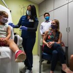 A 6 year old little girl gets a shot of the COVID-19 vaccine while her family watches.