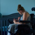 A mother in a wheel chair holds her baby in her arms.