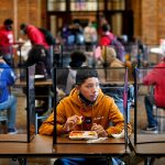 Students eat lunch separated from classmates by plastic dividers.