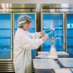 A woman in a lab coat and face shield prepares milk in a laboratory.