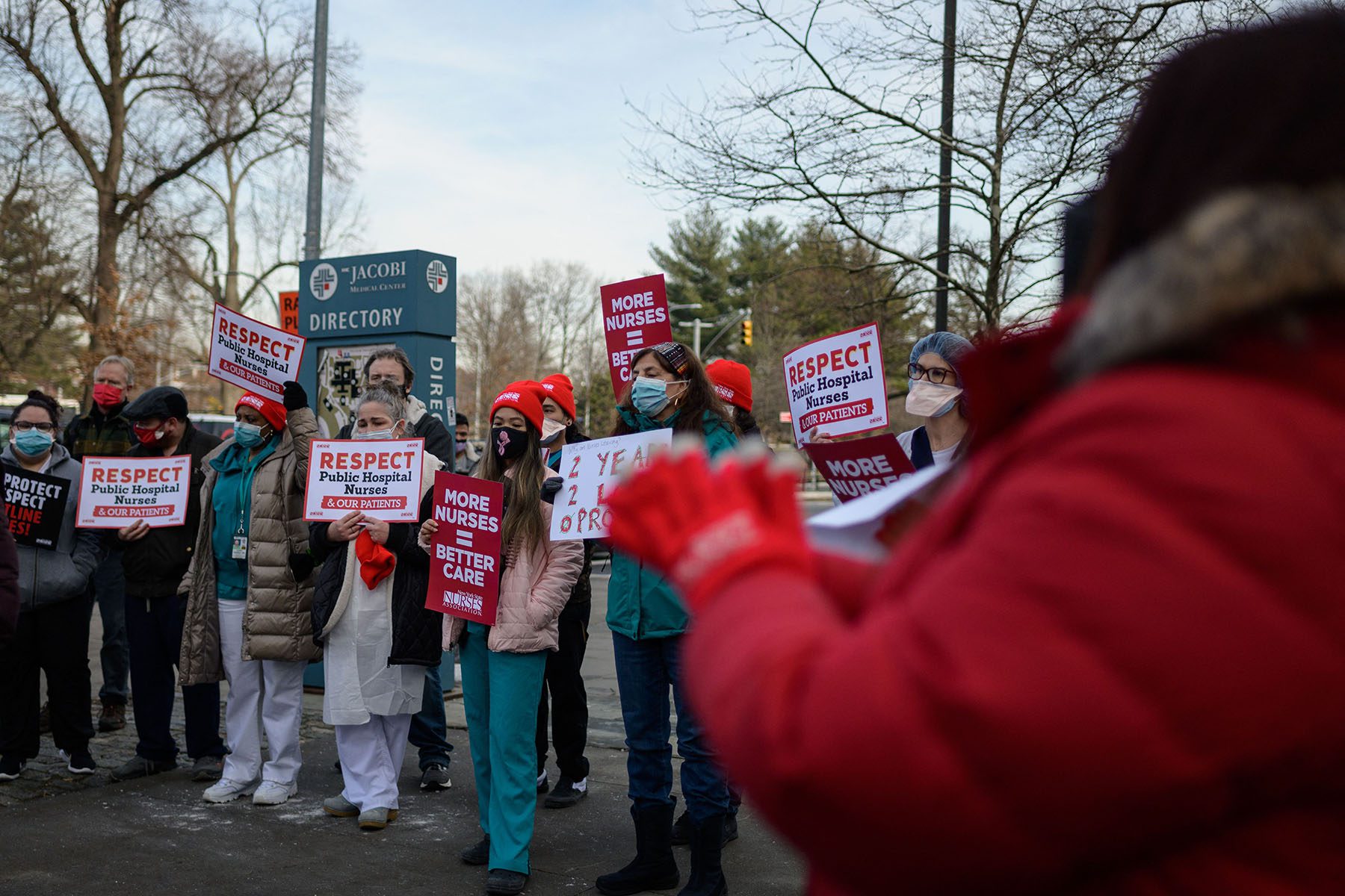 Nurses hold signs that read "Respect public hospital nurses" and "more nurses = better care."