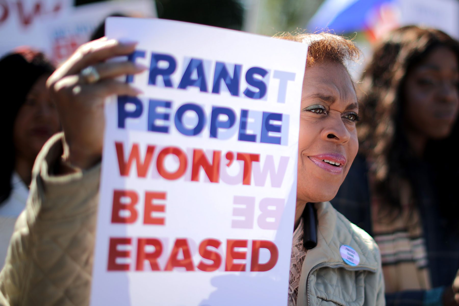 An activist holds a sign that reads "Trans People Won't Be Erased."