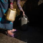 A woman collects water from a source into containers.