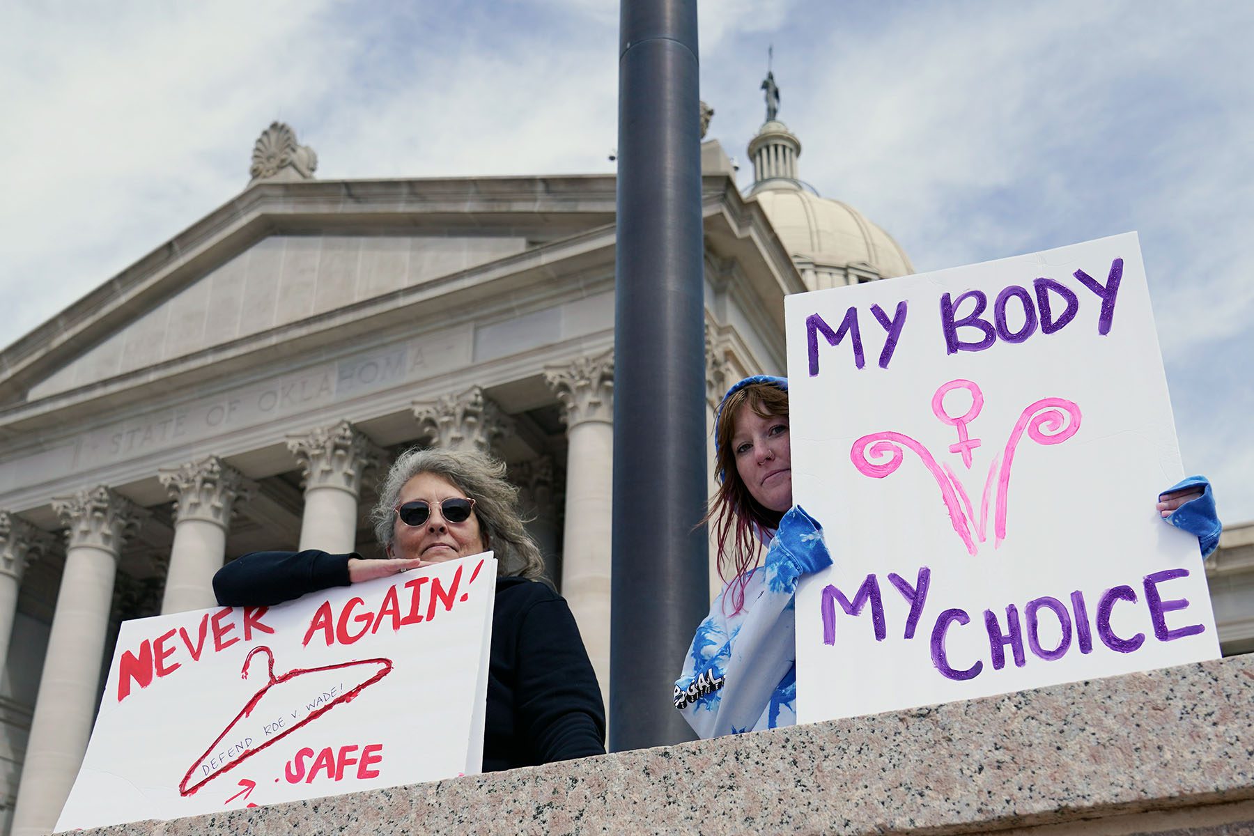 Abortion rights demonstrators hold signs at the Oklahoma state Capitol. One reads "My Body My Choice" and the other reads "Never Again" with a drawing of a clothes hanger.