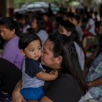 A woman surrounded by people at an evacuation center embraces her young son.