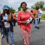 Donna Edwards walks down a street carrying a small pamphlet. Others around her carry signs that read 