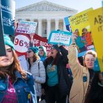 Demonstrators shout slogans and hold banners in front of the Supreme Court.