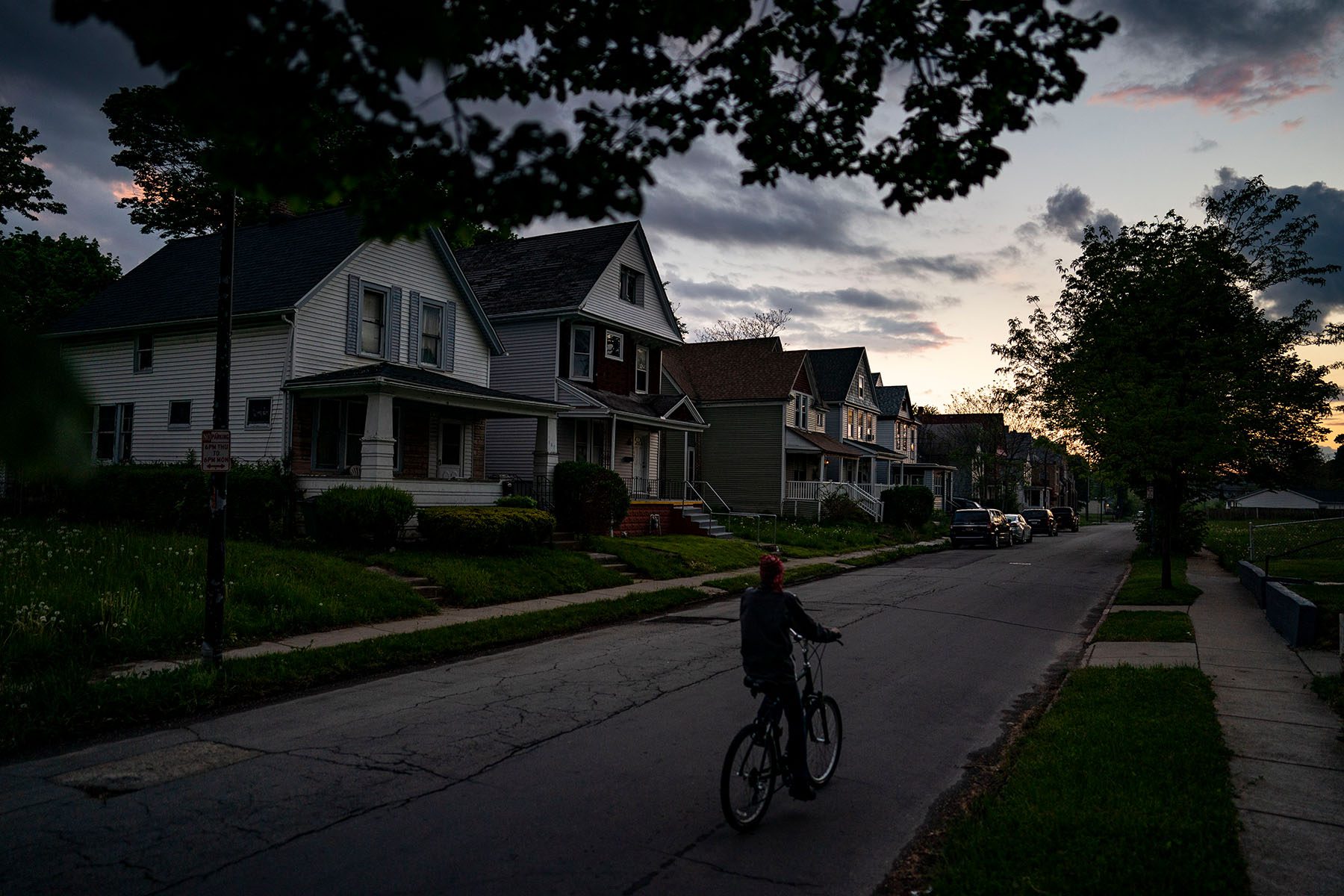 A person rides a bike along a residential street at sunset.