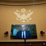 A television mounted on a wall in a Senate hearing room shows Abott Senior President Christopher Calamari as he testifies remotely.