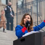 Janice McGeachin stands at a podium and holds a microphone as she speaks on the steps of the Idaho Statehouse.