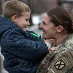 A mother embraces her young son after coming home from Afghanistan. They are both facing each other and smiling.