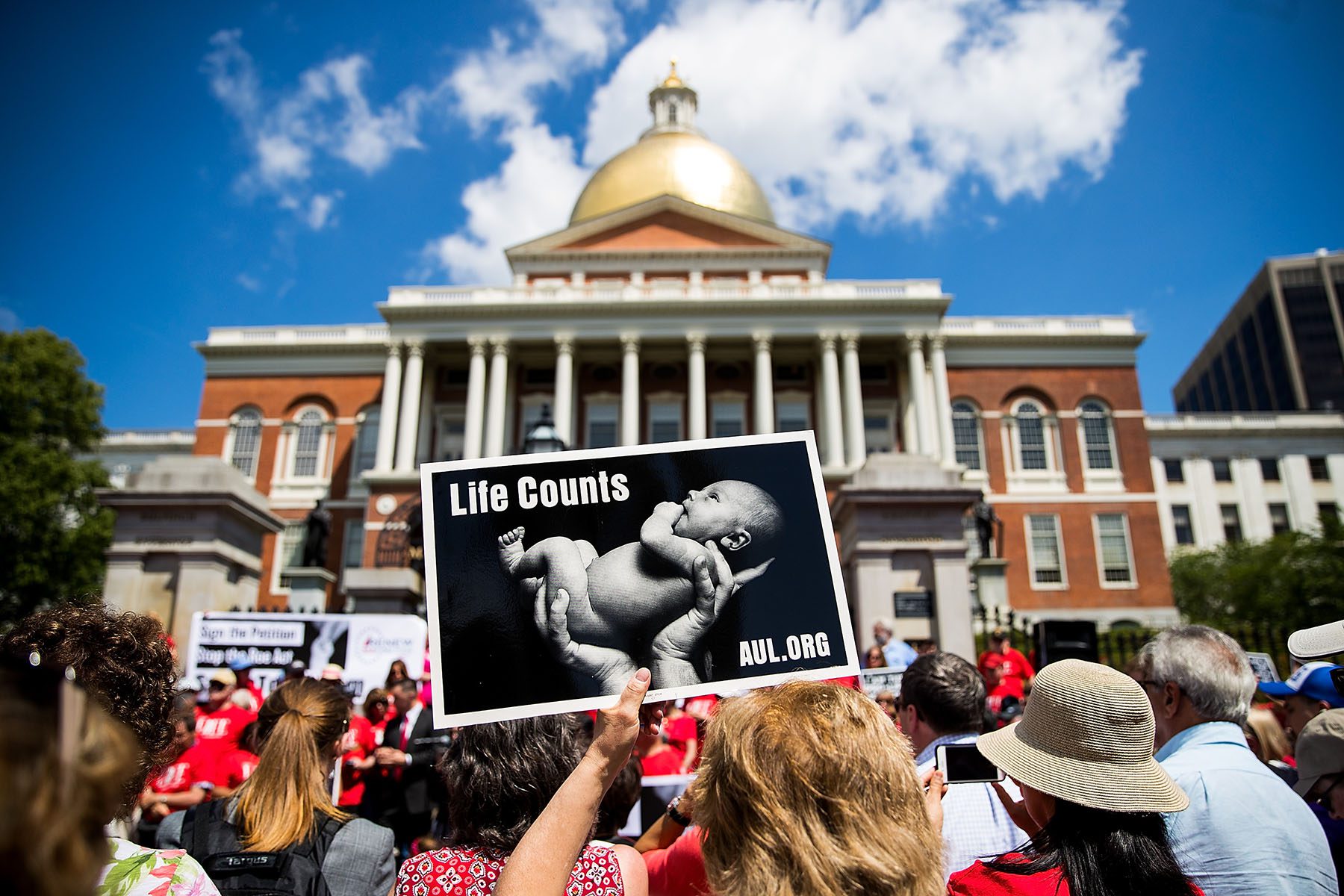 Anti-abortion demonstrators are seen in front of the Massachusetts Statehouse. In the foreground, a protester holds a signs on which an image of a baby is printed with the words "Life Counts" and "AUL.ORG"