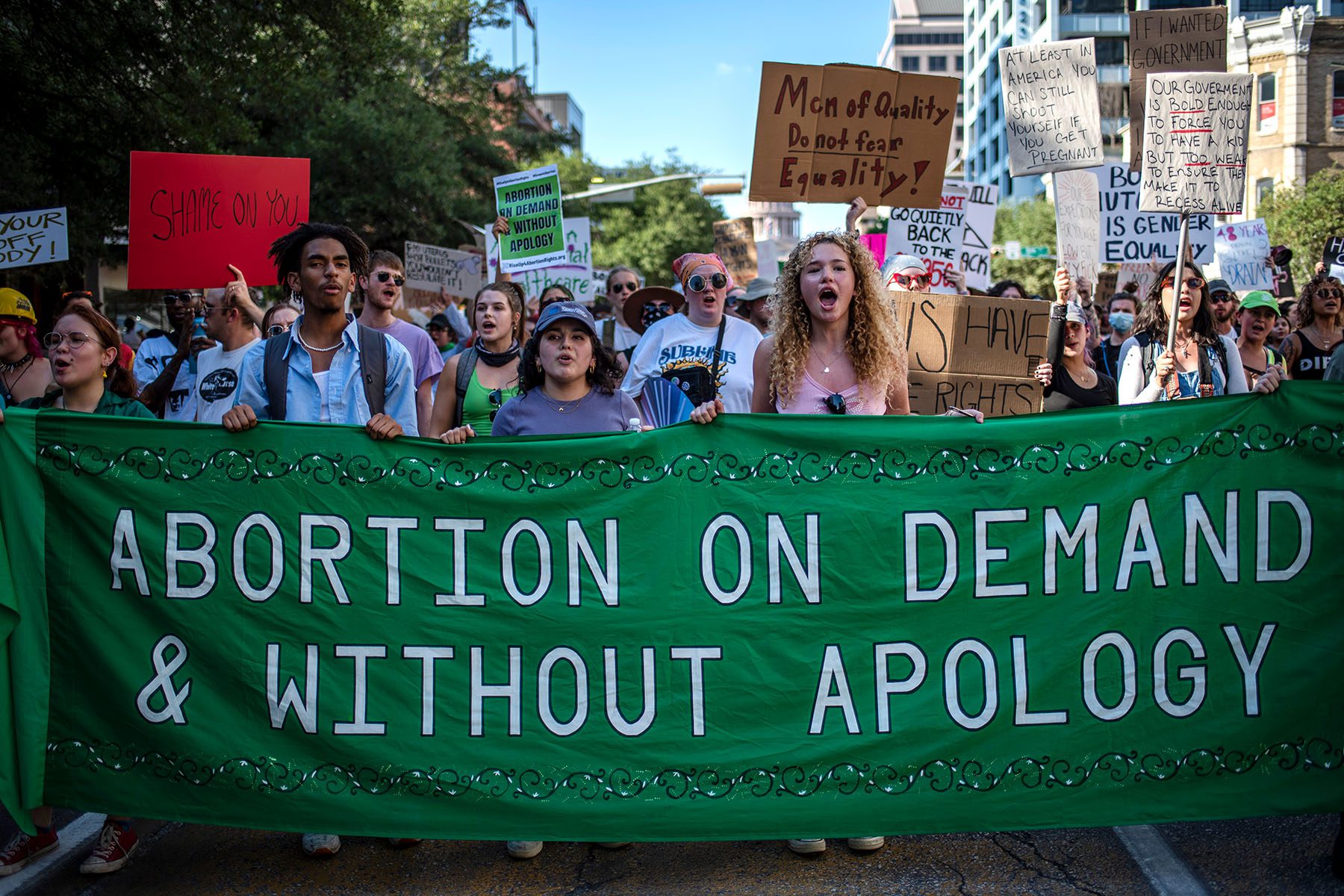 Protesters march while holding signs during an abortion-rights rally. A large banner reads "Abortion on demand & without apology"