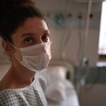 Portrait of genderqueer patient in a doctor's exam room wearing a face mask.