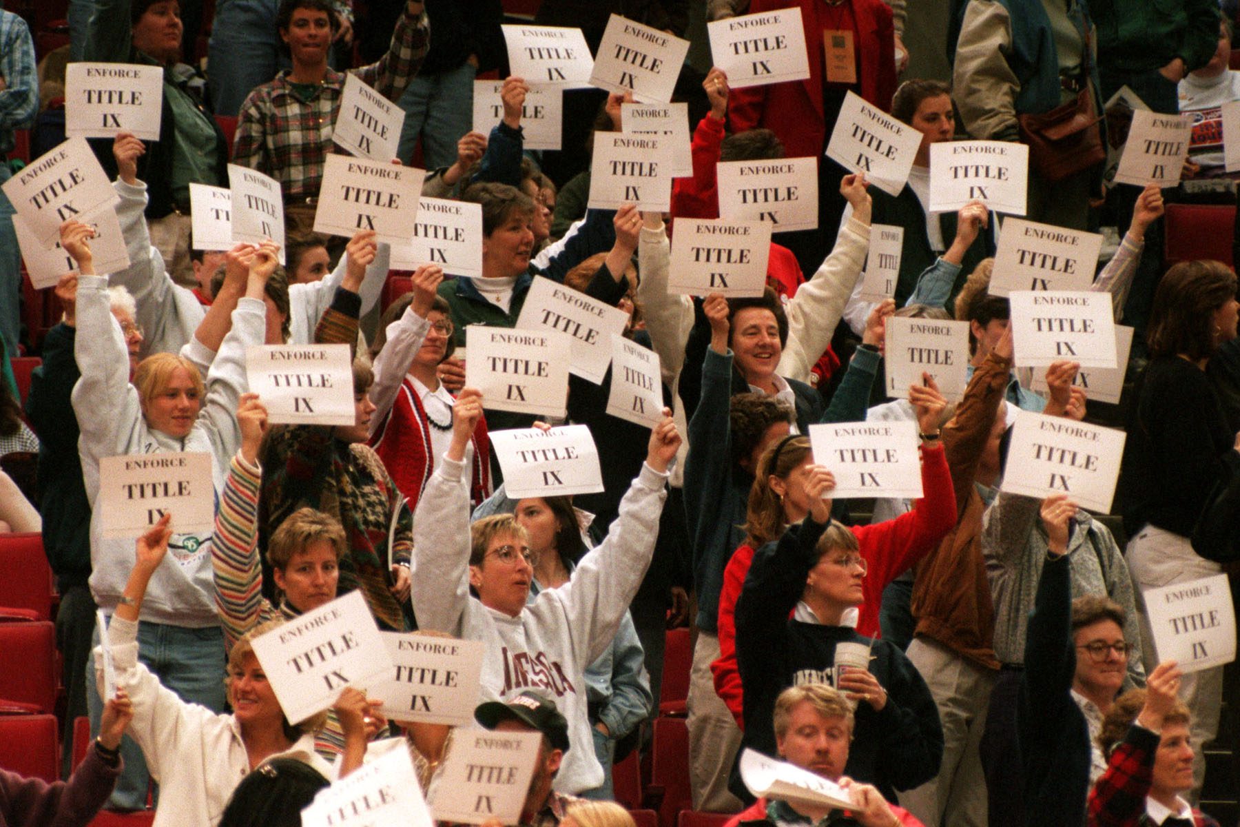 Members and supporters of the Women's Basketball Coaches Association demonstrate in support of Title IX by holding up printed signs that read "Enforce Title IX"