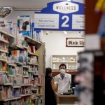 A woman speaks to a pharmacist inside a pharmacy.