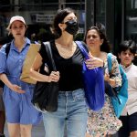 A group of three women walk on a crowded street.