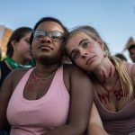 Two friends lean on one another as they look into the distance amidst a demonstration outside the Supreme Court.