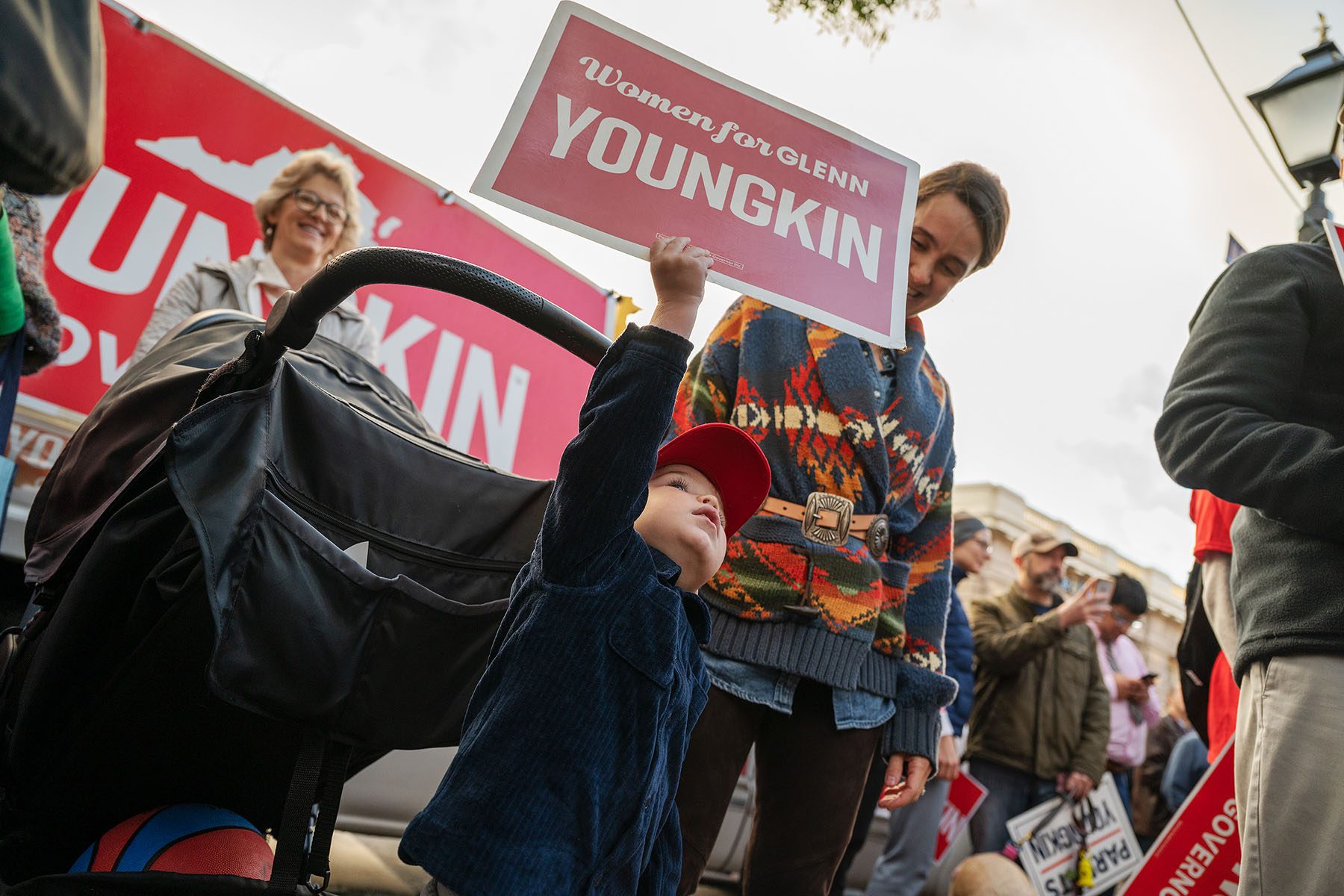 A child holds up a campaign sign tht reads "Women for Glenn Youngkin" at a campaign rally.